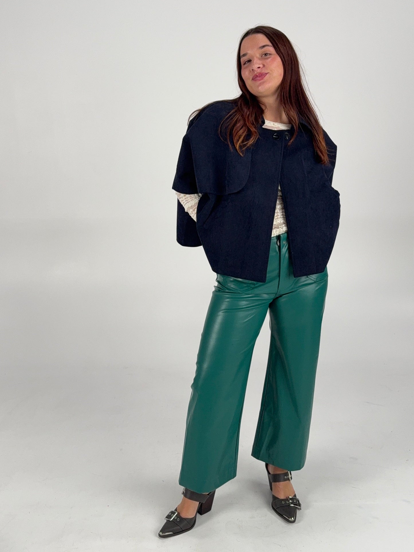 “Chic holiday look featuring green leather pants, white lace blouse, and navy poncho — modern boutique style.”